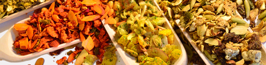Close-up of assorted dried vegetables and seeds in white trays, arranged in colorful rows, including orange, green, and brown hues.