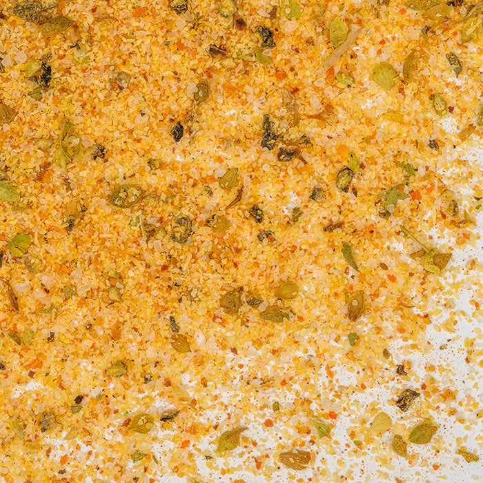 Close-up of Whole Spice Inc. Adobo Seasoning blend with yellow, orange, and green flakes on a white surface—ideal for meat rubs and made with no MSG.