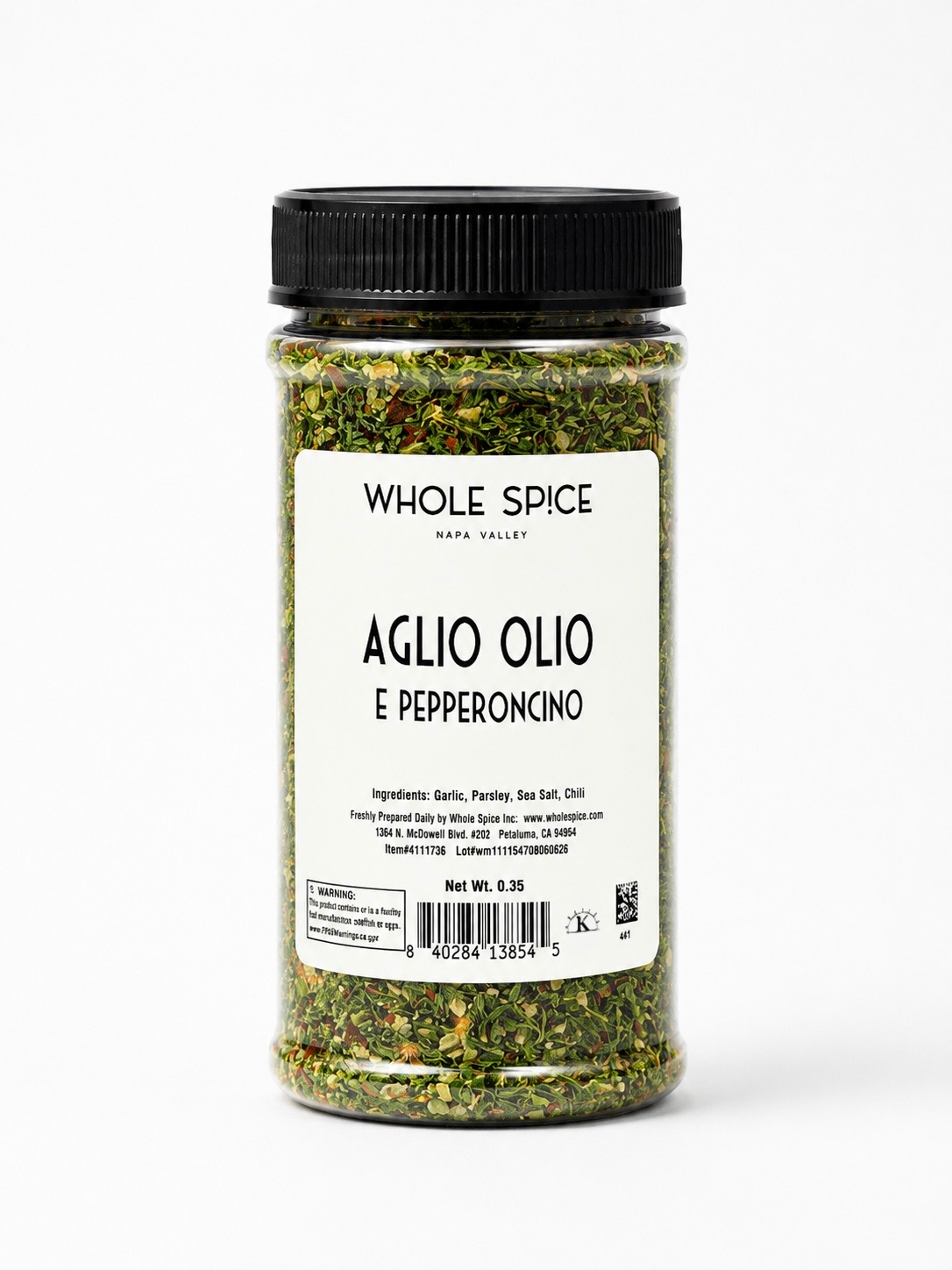 A clear plastic jar from Whole Spice Inc. labeled Aglio Olio E Pepperoncino contains a vibrant blend of green and red Mediterranean spices, topped with a black lid. Showcasing visible ingredients and authentic Italian flavor, this garlic seasoning features a crisp white label with a barcode.