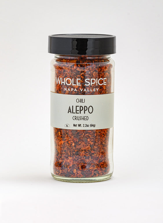 A clear glass jar of Whole Spice Inc. Aleppo Chili Crushed, featuring a black lid and a white label with the product name and weight, photographed on a plain white background.