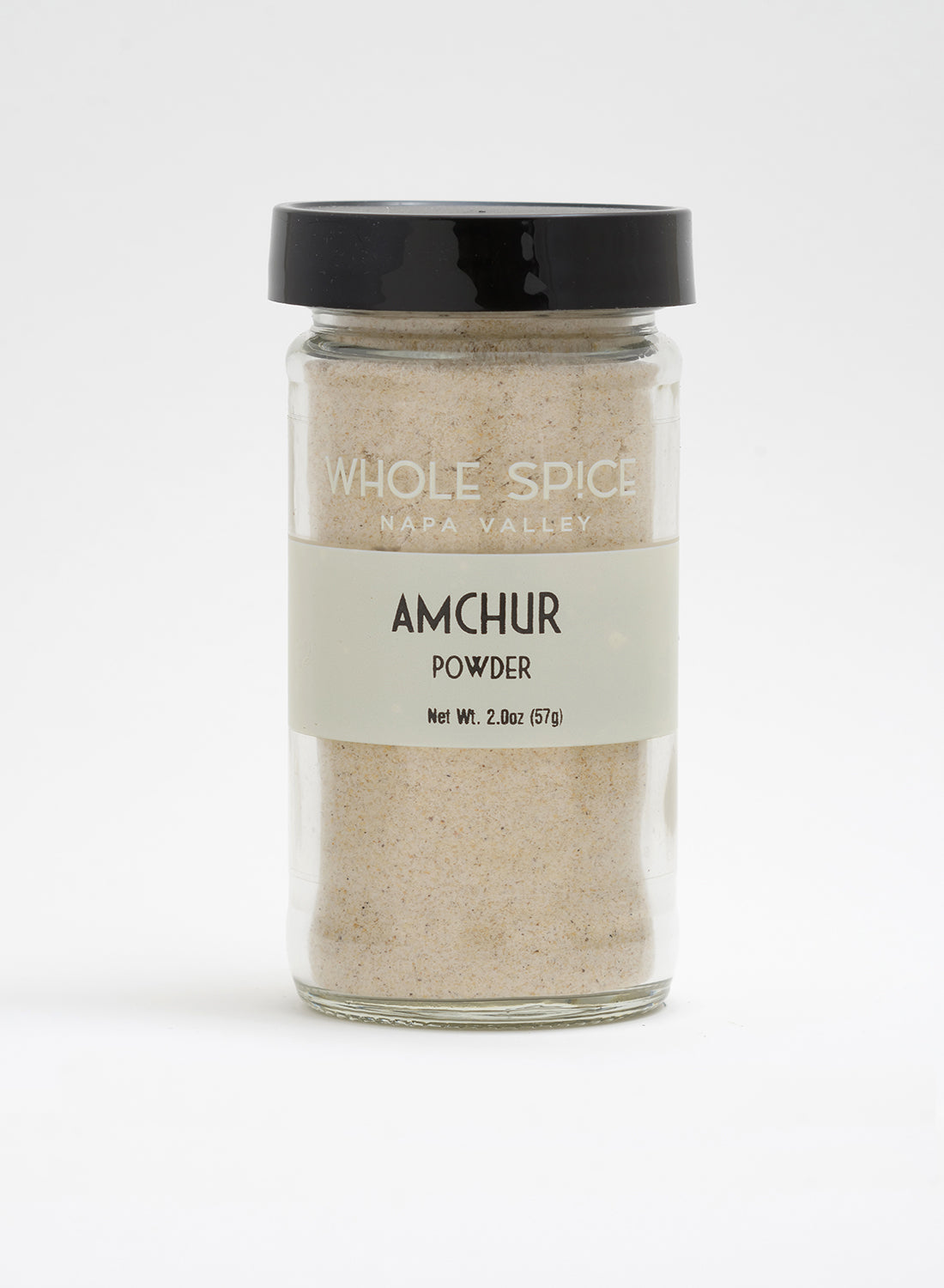 A glass jar with a black lid labeled "Whole Spice Inc. Amchur Powder," Net Wt. 2.0oz (57g), filled with light beige mango powder, shown against a plain white background.