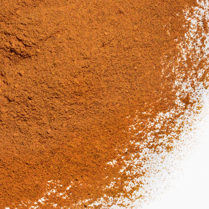 A close-up of a pile of Whole Spice Inc. Annatto Powder — Clearance shows the reddish-brown powder, spread across a white background with scattered edges, highlighting its natural coloring.