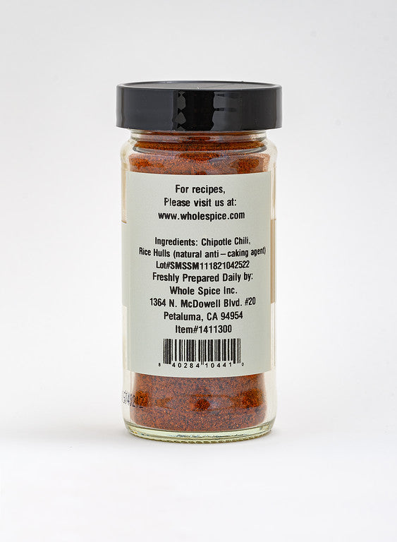A glass jar of Whole Spice Inc. Chipotle Chili Powder with a black lid features a label listing ingredients, manufacturer info, website, address, lot number, and barcode—perfect for adding smoky flavor to Mexican dishes.