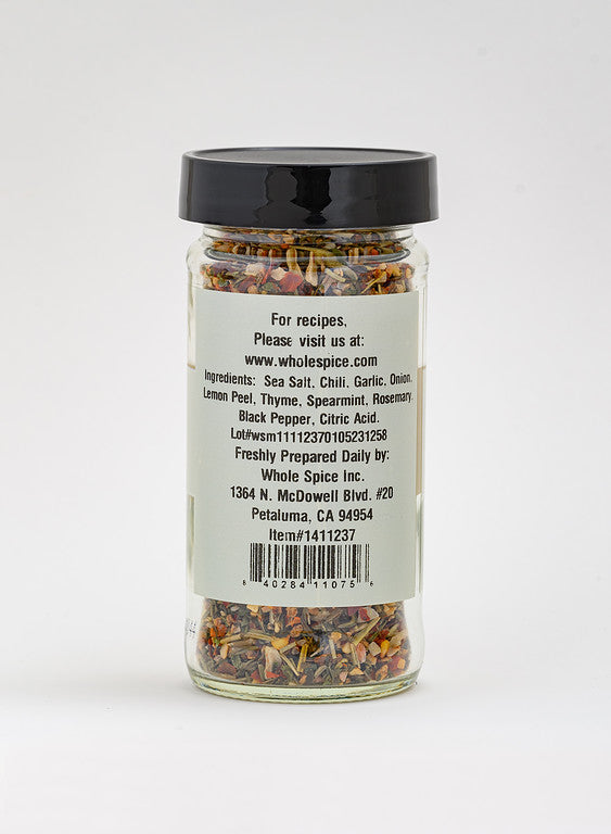 A clear glass jar with a black lid holds Whole Spice Inc.'s Lamb Rub, featuring Mediterranean spices such as sea salt, chili, garlic, thyme, and rosemary. The label displays company info and the website.