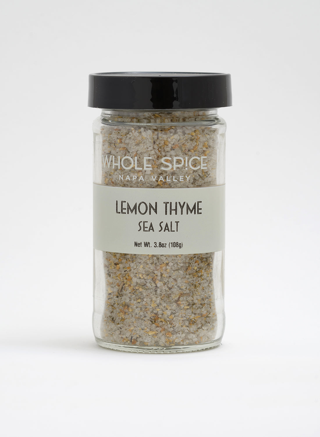 A clear glass jar with a black lid holds Whole Spice Inc. Lemon Thyme Sea Salt (3.8 oz/108g). The white label displays the product name and weight, making it perfect as a finishing salt.