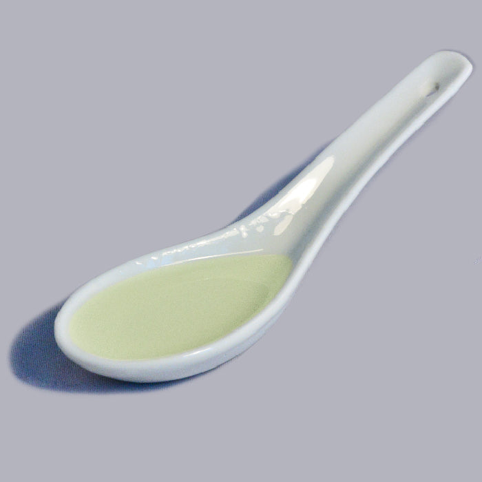 A white ceramic spoon with a small amount of pale yellow Whole Spice Inc. Orange Extract Organic rests on a light gray surface, casting a soft shadow.