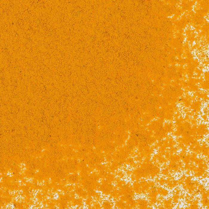 A close-up of Whole Spice Inc. Turmeric Powder—a key ingredient in Indian cuisine—shows its vibrant yellow-orange color and fine texture scattered across a white surface.