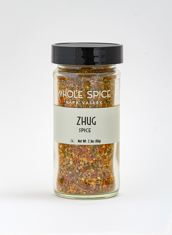 A 2.3 oz (65g) glass jar with a black lid from Whole Spice Inc., labeled Zhug Spice, holds a colorful Yemenite blend of dried herbs and spices for a hot zhug spice mix.