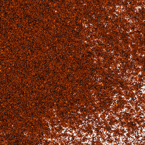 A close-up of Whole Spice Inc. Ancho Chili Powder sprinkled over a white surface, highlighting the rich texture and depth it brings to Mexican dishes like mole.