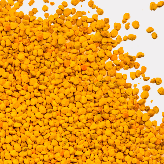 A close-up of golden-yellow Bee Pollen granules from Whole Spice Inc. scattered on a light surface—a nutrient-rich superfood commonly used as a dietary supplement.