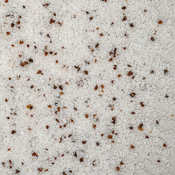 Close-up of coarse white Black Truffle Salt by Whole Spice Inc., mixed with small, irregular brown and reddish pepper flakes, scattered across the surface for a premium gourmet touch.