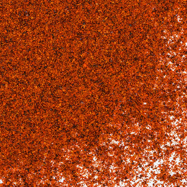 A close-up of vibrant red-orange Whole Spice Inc. Chipotle Chili Powder, known for its smoky flavor, scattered on a white surface—a key ingredient in Mexican cuisine.