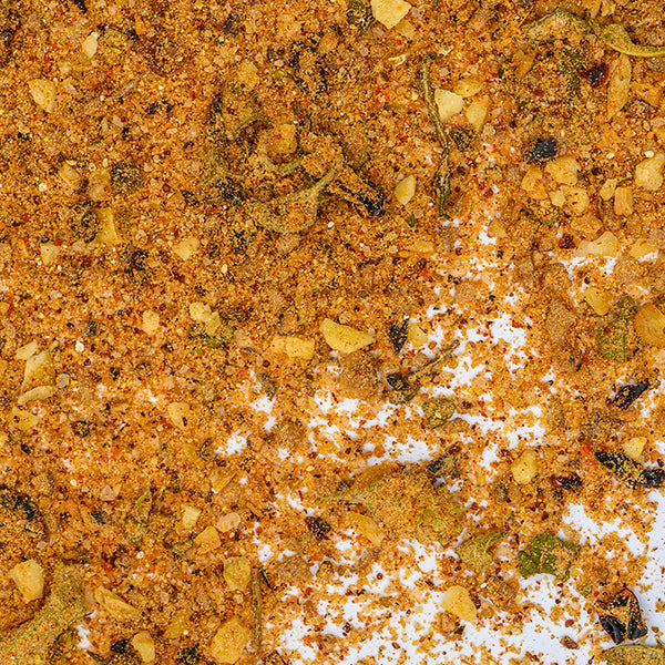 A close-up of Whole Spice Inc.'s Chipotle Honey Rub, showcasing its coarse blend of chili, garlic, herbs, and hickory smoked sea salt scattered across a flat surface.