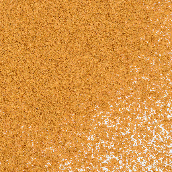 A close-up of brown sugar on a white surface, sprinkled with Cinnamon Powder Ceylon by Whole Spice Inc., with granules and a touch of cinnamon unevenly scattered in the lower right corner.