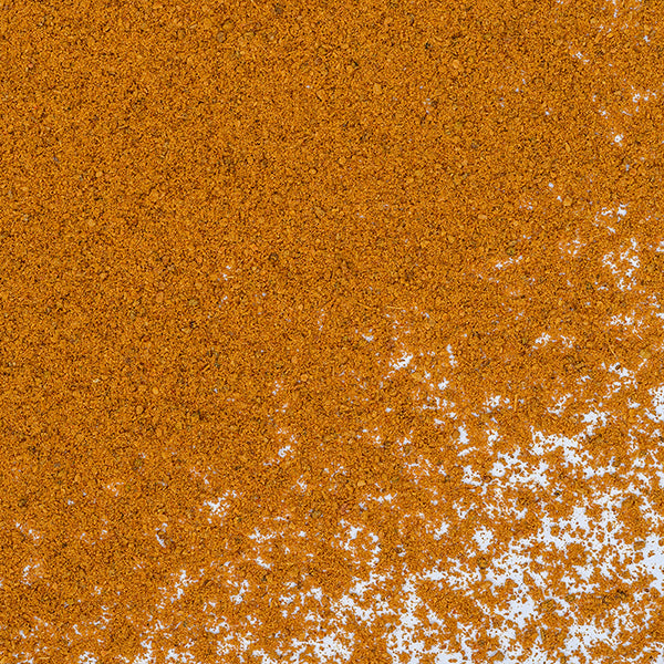 A close-up of Cinnamon Powder Saigon by Whole Spice Inc. scattered on a white surface, densely packed in the upper left and gradually thinning toward the lower right.