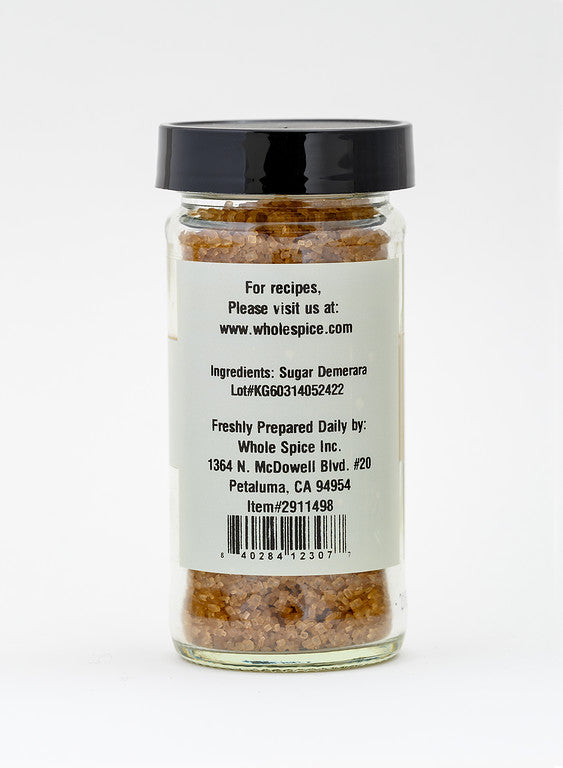 A clear glass jar of Whole Spice Inc. Demerara Sugar features rich molasses crystals and a black screw-on lid. The back label details ingredients, company info, and a website for recipes.