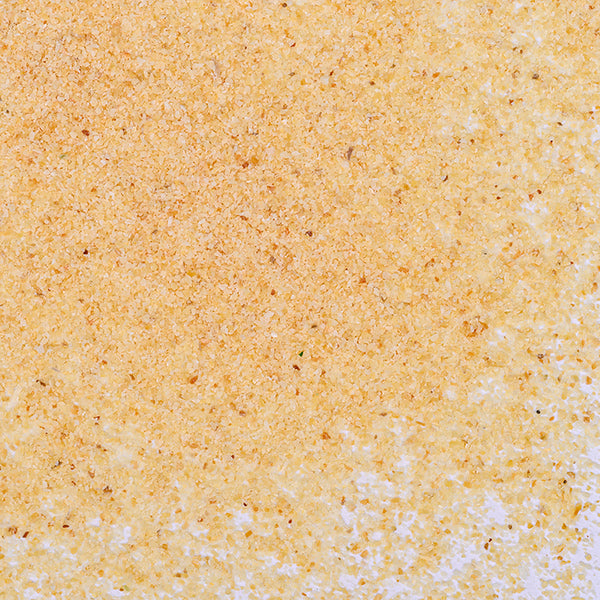 Close-up view of Whole Spice Inc. Garlic Granulated—a scattered pile of fine, light brown granules on a white surface, resembling garlic seasoning or dehydrated garlic.