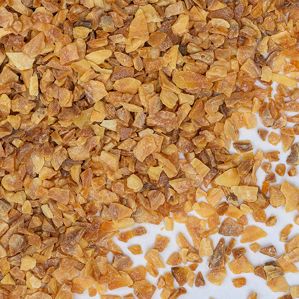 A close-up of Whole Spice Inc. Garlic Roasted Chopped shows golden brown flakes scattered on a white surface, ideal for Mediterranean dishes and perfect to pair with your favorite seasonings.