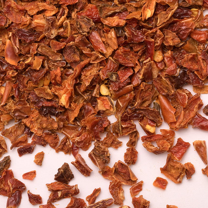 A close-up of Whole Spice Inc. Jalapeño Red Chili Diced scattered on a light surface, featuring varied reddish-brown and orange pieces—ideal for adding bold flavor to your chili stew.