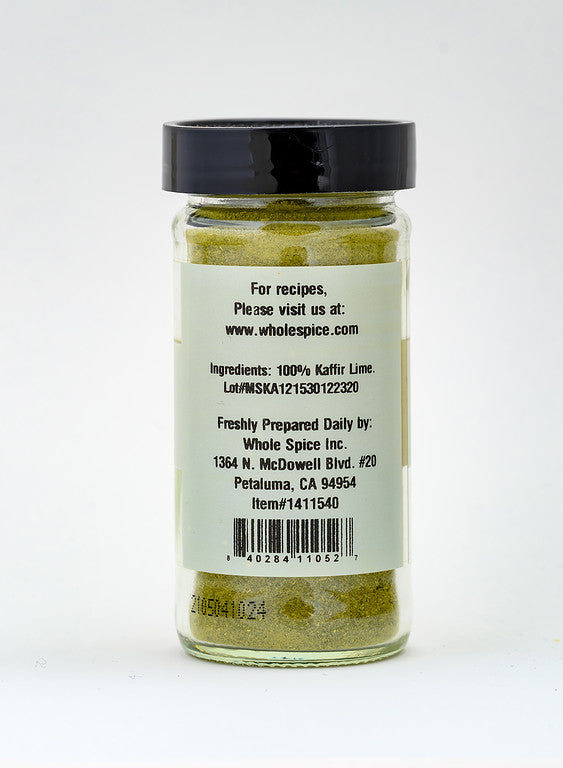 A clear glass jar of Whole Spice Inc. Kaffir Lime Powder with a black lid reveals green powder inside. The back label lists ingredients, origin, a recipe website for Asian cuisine, and a barcode at the bottom.