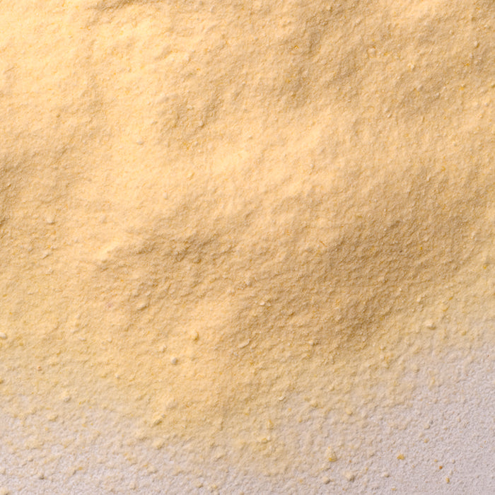 Close-up of light yellow, finely ground Whole Spice Inc. Mango Fruit Powder spread unevenly on a white surface, highlighting its textured look—ideal for adding tropical flavor to snack mixes.