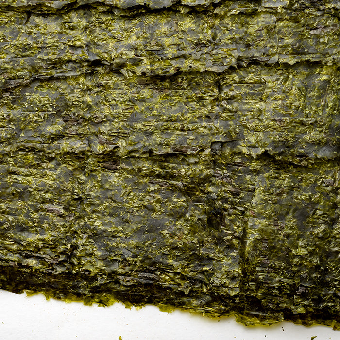 Close-up of Whole Spice Inc. Roasted Seaweed Yakisushinori, showing its crinkled, textured dark green sheet with hints of yellow on a white background.