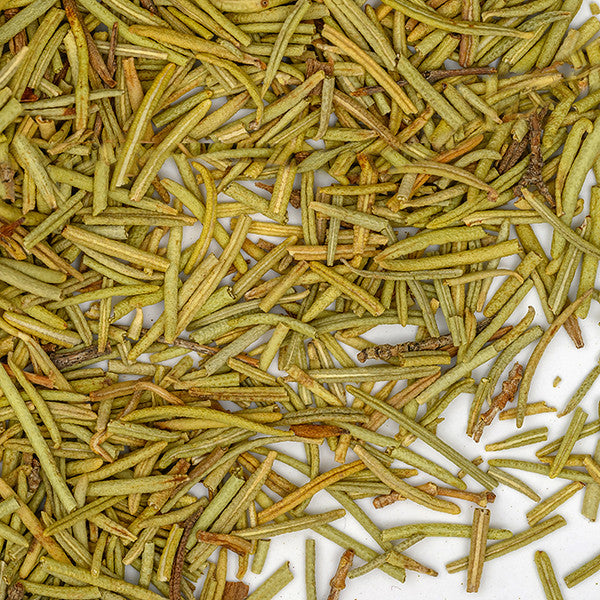 Close-up of Rosemary Organic by Whole Spice Inc.—dried, needle-like leaves scattered on a white surface, displaying their signature yellowish-green color and highlighting this classic Mediterranean herb.