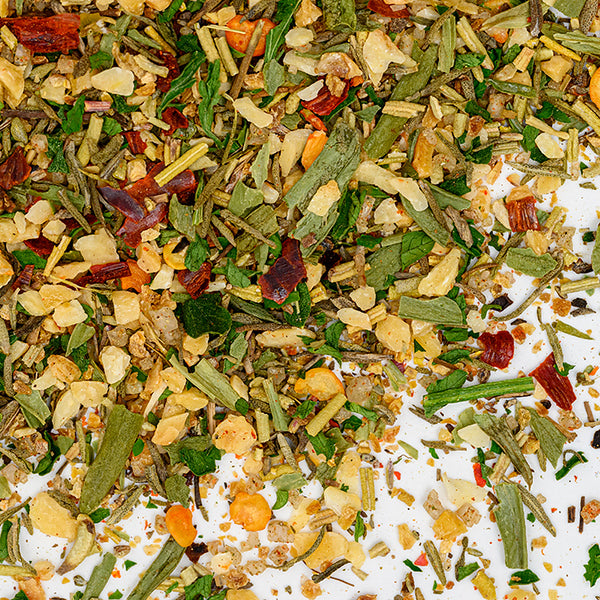 A close-up of Whole Spice Inc. Rotisserie Chicken Rub shows a vibrant blend of chopped green herbs, red chili flakes, and yellow garlic or onion bits—perfect for adding flavor to rotisserie chicken.