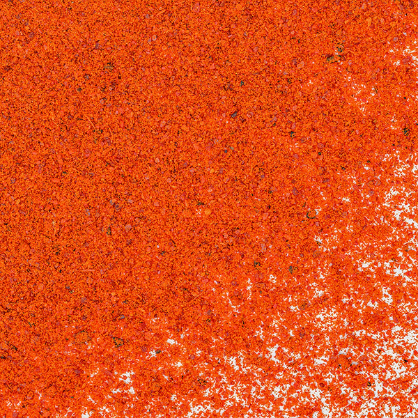 A close-up of vibrant red-orange Tagine Spice by Whole Spice Inc., scattered on a white surface, evokes the rich Moroccan flavors found in traditional tagine seasoning blends.