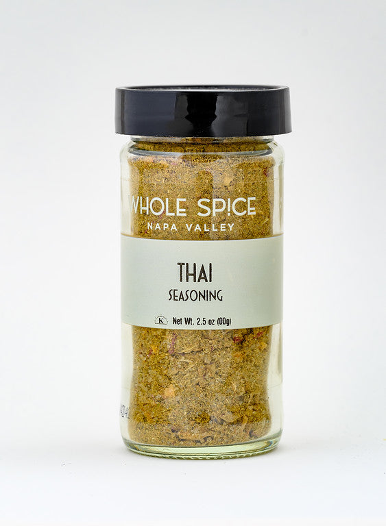 A clear glass jar with a black lid contains yellow-green Thai Seasoning from Whole Spice Inc., Net Wt. 2.5 oz (100g), perfect for adding bold flavor to authentic Thai dishes, shown against a plain white background.