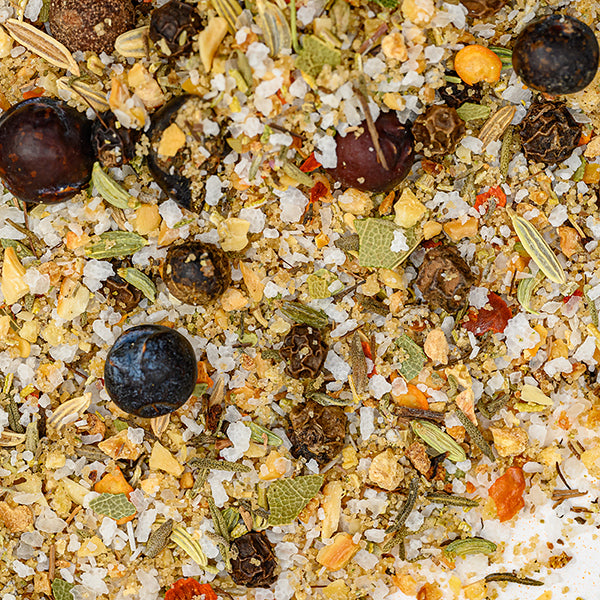 Close-up of Whole Spice Inc. Turkey Brining Blend—a colorful mix of coarse salt, dried herbs, seeds, peppercorns, and dried veggies—perfect as a turkey brine or seasoning, scattered across a white surface.