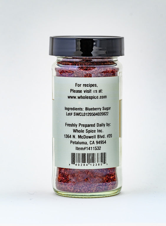 A clear glass jar with a black lid holds Wild Blueberry Sugar. The label shows the Whole Spice Inc. brand, lists Wild Blueberry Sugar as the ingredient, and includes contact details plus a lot number.