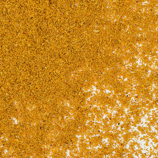 A close-up of Yellow Indian Curry Powder by Whole Spice Inc. shows the yellowish-orange blend of curry spices scattered unevenly across a white surface.