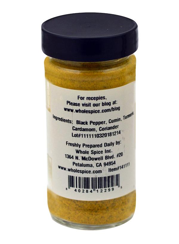 A spice jar labeled "Afghan Ribs Blend" by Whole Spice Inc. displays its back label: ingredients—black pepper, cumin, turmeric, cardamom, coriander—perfect for grilling. Company info and blog details appear above the barcode.