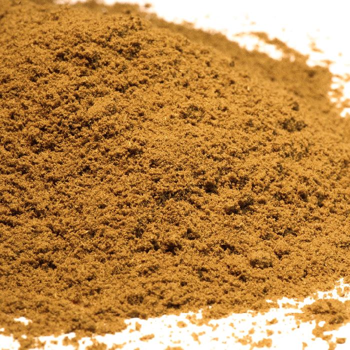 A close-up of finely ground Ajwain Seed Powder by Whole Spice Inc., spread out on a white surface, showcasing its brown color and fine texture for Indian cooking.
