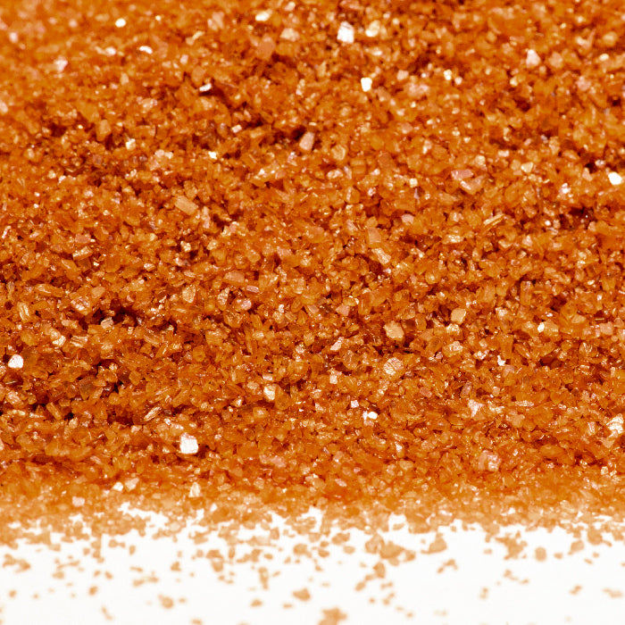 A close-up shows coarse, orange-brown crystals of Whole Spice Inc. Alaea Hawaiian Sea Salt spread on a white surface, resembling colored sugar.