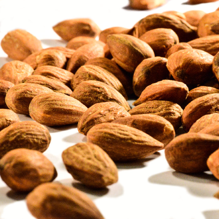 A close-up of Whole Spice Inc. Almonds Unsalted Roasted scattered on a white surface, featuring their rough, textured brown shells and showcasing this healthy snack in various orientations.