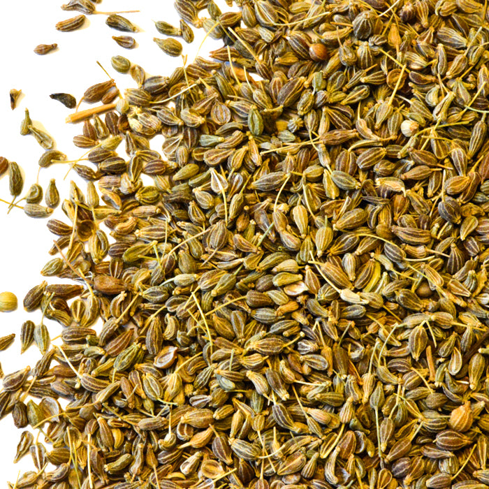 A close-up of Whole Spice Inc. Anise Seed, with small, light brown, oval seeds scattered on a white background—renowned for their licorice flavor, perfect for enhancing Moroccan cookies and sweet dishes.