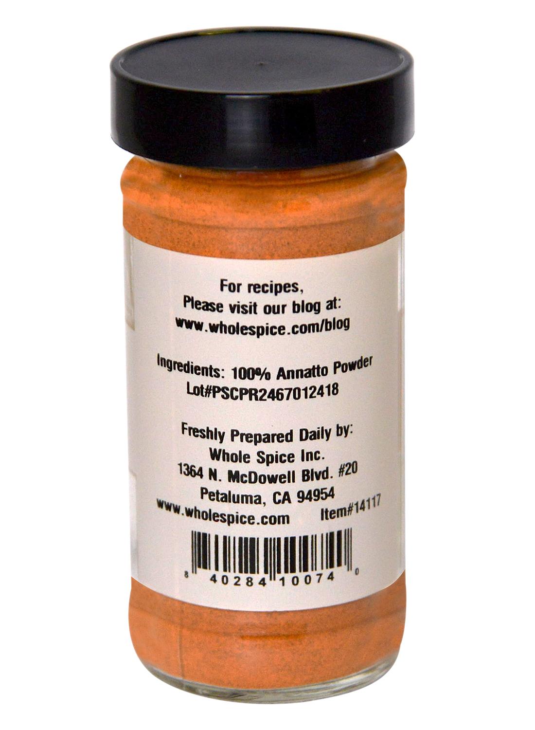 A clear spice jar of Whole Spice Inc. Annatto Powder contains 100% pure achiote seed for natural coloring, features ingredient details, lot number, company address in Petaluma, CA, recipe website on the label, and comes with a black lid.