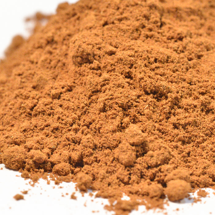 A close-up of finely ground Apple Pie Seasoning by Whole Spice Inc., a versatile brown spice, spread on a white surface.
