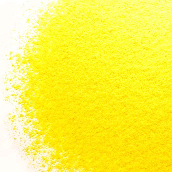 A close-up of Whole Spice Inc. Asafoetida Powder, a vibrant yellow Indian flavor enhancer, scattered on a white surface with color intensity fading toward the edges.
