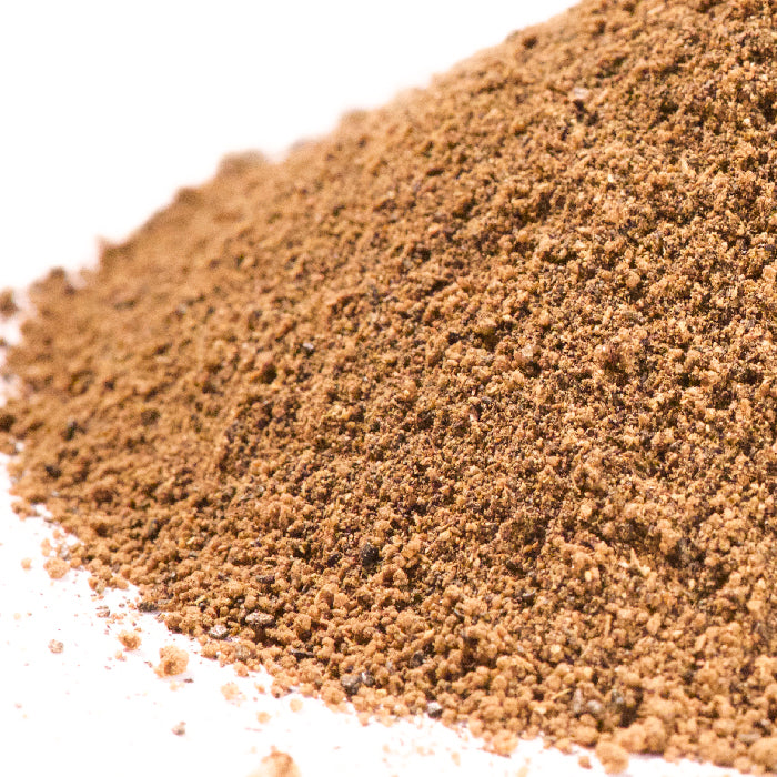 A close-up of Whole Spice Inc.’s Asian Smoked Tea Rub—a finely ground brown powder with a granular texture—scattered on a white surface, perfect for adding bold, exotic Lapsang Souchong Tea flavor to your dishes.