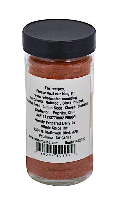 A clear glass jar of Baharat Spice by Whole Spice Inc. with a black lid and red spice blend. The white label shows ingredients, prep details, barcode, and distributor address. The front isn’t visible. Ideal for Gulf States cuisine.