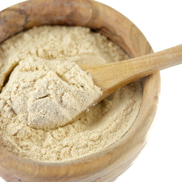 A wooden bowl of Whole Spice Inc. Balsamic Vinegar Powder, light beige in color, with a wooden spoon partially buried in the seasoning. Set against a white background.