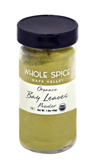 A clear glass jar with a black lid labeled Whole Spice Inc. Bay Leaves Ground Organic, Net Wt. 1.6oz (45g), containing greenish ground bay leaves from laurus nobilis.