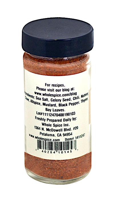 A glass jar of Whole Spice Inc. Bay Seafood Seasoning with a black lid features a label listing sea salt, celery seed, chili, nutmeg, and more. The label also includes the company address and website for recipes.