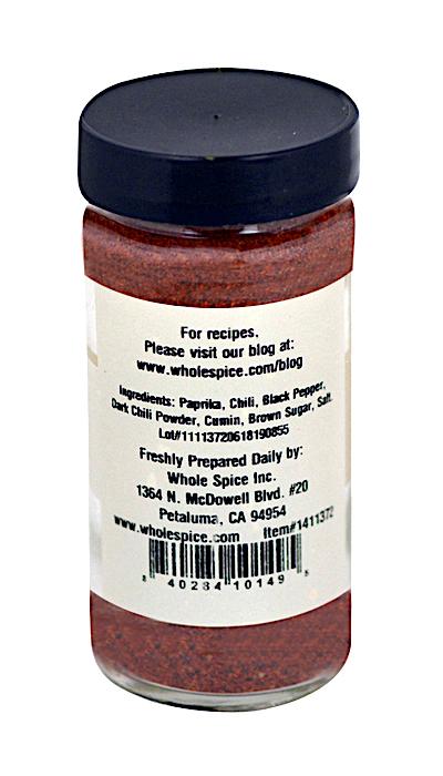 A clear spice jar from Whole Spice Inc. labeled “BBQ Rub” with a black lid, back label listing paprika, chili, pepper, cumin, company info and website. The reddish-brown BBQ Rub is ideal for grilling or as a meat rub.