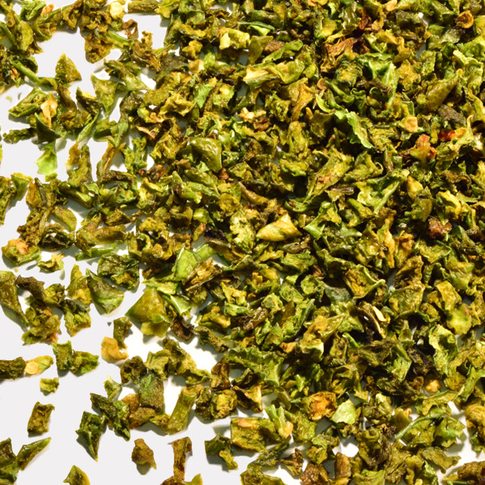 Close-up of Whole Spice Inc. Roasted Green Bell Pepper Diced scattered on a white surface, showcasing their chopped texture and vibrant green color.