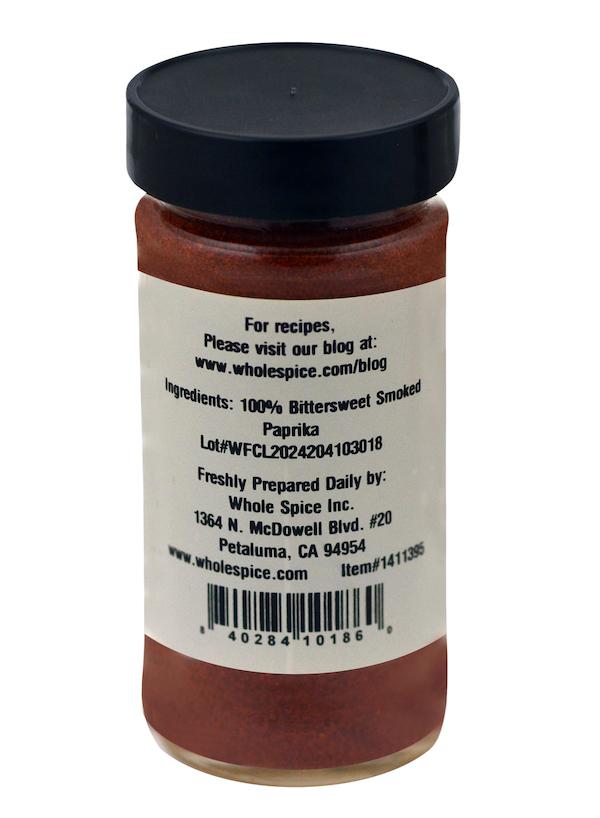 A clear spice jar with a black lid contains Whole Spice Inc. Bittersweet Smoked Paprika, 100% pure red powder celebrated for its deep Spanish flavor. The label also lists the company’s contact details.