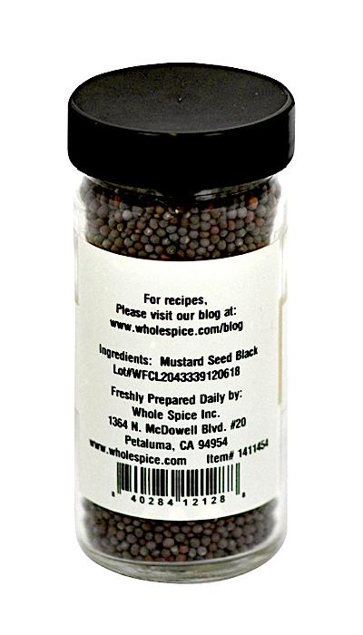 A clear spice jar with a black lid from Whole Spice Inc. contains Black Mustard Seed Whole. The label lists the ingredient as mustard seed black and includes company contact info plus a website for recipes.